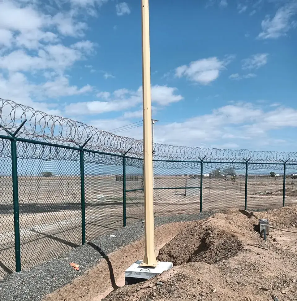Perimeter lighting pole installed behind security fence